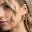 A close-up of a woman's ear wearing a textured gold huggie hoop earring, with her blonde hair framing the side of her face.