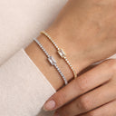 Two delicate tennis-style bracelets with rectangular bezel-set clear stones, one in yellow gold and one in silver, worn on a person's wrist against a soft cream knit background.