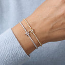Two delicate star-themed bracelets on a person's wrist, one in yellow gold and one in silver, both featuring pavé-set clear stones. The person is wearing a light blue ribbed sweater against a soft gray-blue background.