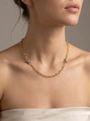 A close-up of a model wearing a delicate gold chain necklace with small silver star-shaped charms, styled with a soft beige satin strap against a neutral gray background.