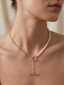 A close-up of a model wearing a delicate gold necklace with a white pearl strand and a T-bar clasp pendant.