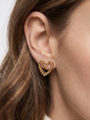 A close-up of a model's ear wearing a gold heart-shaped stud earring with a textured, beaded outline.