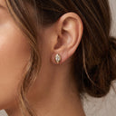 A close-up of a woman's ear wearing a small gold stud earring with a marquise-cut clear gemstone.