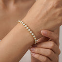 A delicate gold bracelet with small white pearl-like beads worn on a person's wrist, shown in a close-up lifestyle shot.