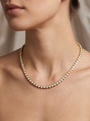 A close-up of a model wearing a delicate gold necklace adorned with small, round white pearls.