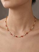 A gold chain necklace with alternating red faceted gemstones and small clear stones, worn on a model's neck against a neutral gray background.
