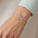 Two snake-shaped bracelets with small green stone accents, one in silver and one in yellow gold, both set with clear stones, shown worn on a person's wrist.