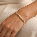 A delicate gold chain bracelet with small, polished oval links, worn on a person's wrist against a soft beige linen background.