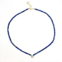 A beaded necklace made of small dark blue lapis lazuli-style beads with gold-toned metal findings, including a clasp and a small heart-shaped charm, shown on a plain white background.