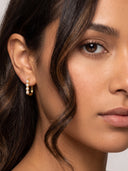 A close-up of a woman wearing a small gold huggie hoop earring adorned with three small white pearls on the lobe of her ear.