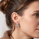 A close-up side profile of a woman wearing a small silver teardrop-shaped stud earring with a textured, diamond-like pattern.