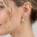 A close-up of a woman's ear wearing a gold geometric pyramid drop earring with a textured, ribbed surface.