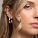 A close-up of a woman wearing a polished silver hoop earring, showing the earring on her ear against her blonde hair and skin.