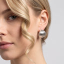 A close-up of a woman's ear wearing a textured, metallic silver post drop earring against a light gray background.