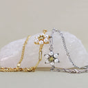 Two delicate chain bracelets displayed on a pale stone surface. One bracelet is gold-toned with a flower-like charm featuring white faux pearls and a small yellow center.