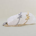 Two delicate curved stretch bracelets with butterfly-shaped crystal clusters, one in yellow gold and one in silver-tone metal, displayed on a white textured stone against a warm beige background.