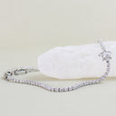 A silver tennis bracelet with a star charm, set with clear stones, displayed on a white crystal cluster against a light beige background.