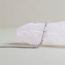 A silver tennis bracelet with clear pavé-set stones draped over a white crystal display on a neutral beige background.