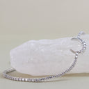 A silver-toned open hoop bangle bracelet, partially unrolled, covered with small clear cubic zirconia stones. It is displayed on a white crystal cluster against a soft beige background.