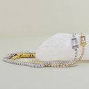 Two tennis-style bracelets displayed on a pale stone against a soft beige background. One bracelet is yellow gold with clear stones, and the other is silver with clear stones.