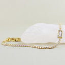 A gold tennis bracelet with clear pavé stones and a rectangular clear gemstone pendant, displayed on a white crystal cluster against a light beige background.