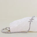 A silver tennis bracelet with a star-shaped charm, displayed on a white crystal block against a light beige background.