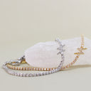 Two delicate tennis bracelets with star-shaped links, one in silver with clear stones and one in gold with clear stones, displayed on a white crystal against a light beige background.