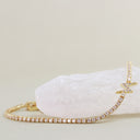 A gold tennis bracelet with clear pavé stones and a small star-shaped charm, displayed on a white crystal against a light beige background.