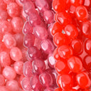 Close-up of glossy oval beads in three colorways: translucent pink, semi-opaque magenta, and bright red-orange, arranged vertically.