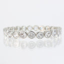 A silver-toned eternity band featuring round brilliant-cut clear stones in bezel settings, displayed on a reflective white surface.