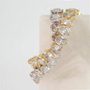 A gold and silver-toned stretch bracelet featuring a row of clear oval-cut gemstones, displayed on a light-colored rectangular stand against a white background.