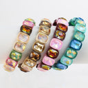 Four colorful beaded bracelets with square faceted rhinestones, displayed on a clean white background. The bracelets feature beads in pink, gold, brown, and blue, with iridescent and metallic finishes.