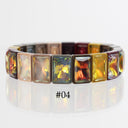 A segmented stretch bracelet featuring rectangular iridescent crystals in a warm gradient of gold, yellow, orange, red, and brown, set in a rose gold-tone metal. The text '#04' is printed below the bracelet on a reflective white surface.